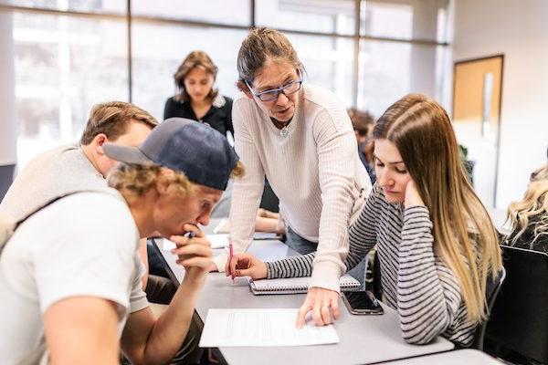 Professor helping several students in a brightly lit classroom.