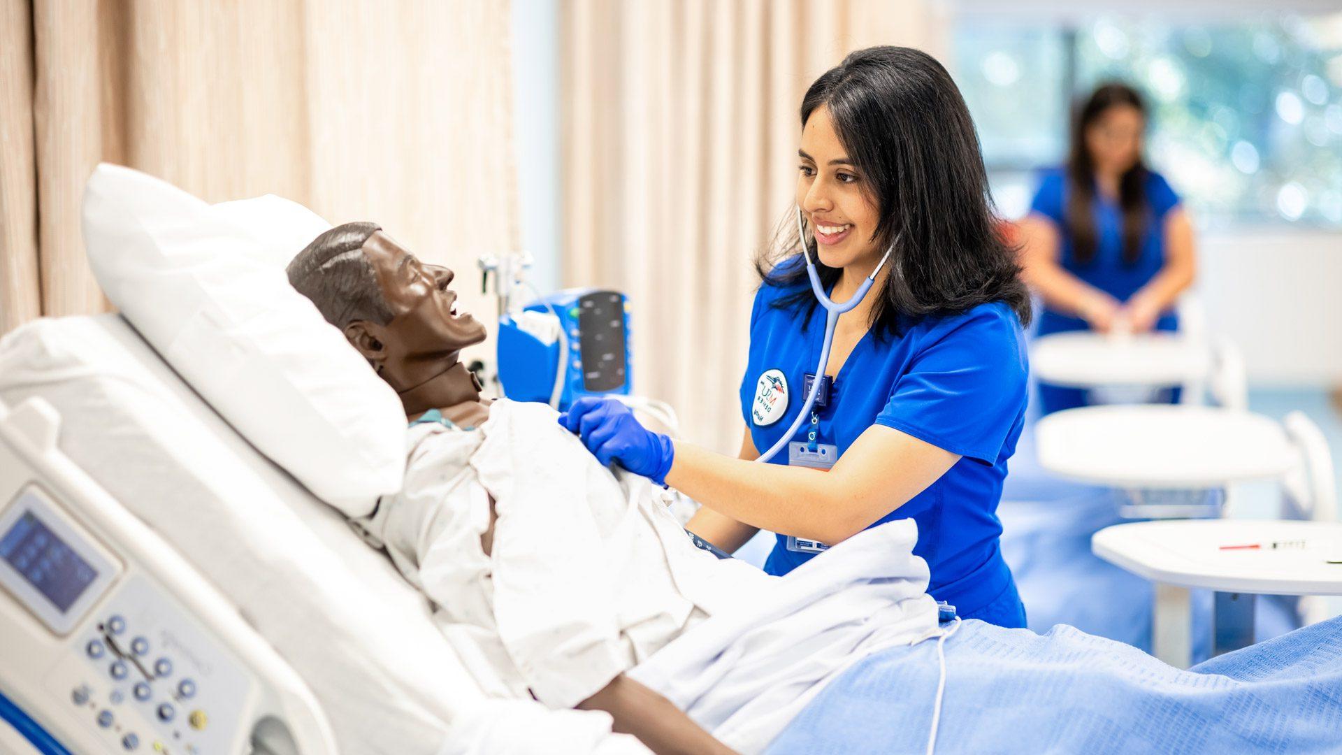 A nursing student in blue scrubs practicing checking vitals on a mannequin in MSU Denver's new Simulation and Skills Lab.